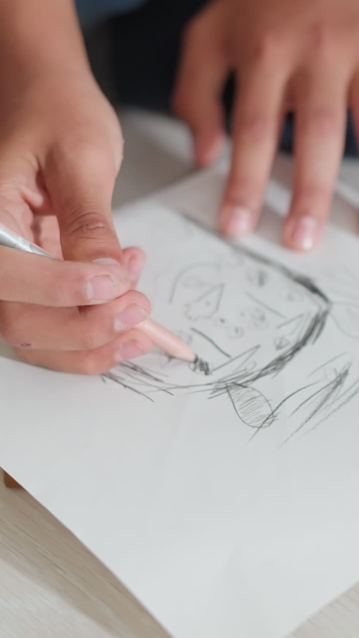 Primer plano de las manos de un niño dibujando con un lápiz sobre un papel blanco apoyado en la tapa de un libro grueso, mostrando un enfoque creativo y habilidades artísticas tempranas con líneas sencillas y formas abstractas.