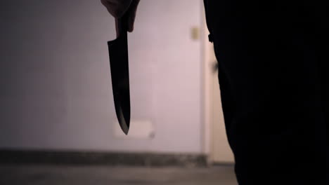 ein gruseliger slasher-killer hält ein küchenmesser als silhouette in der hand und geht in einer hausinvasion in zeitlupe auf sein mordopfer zu