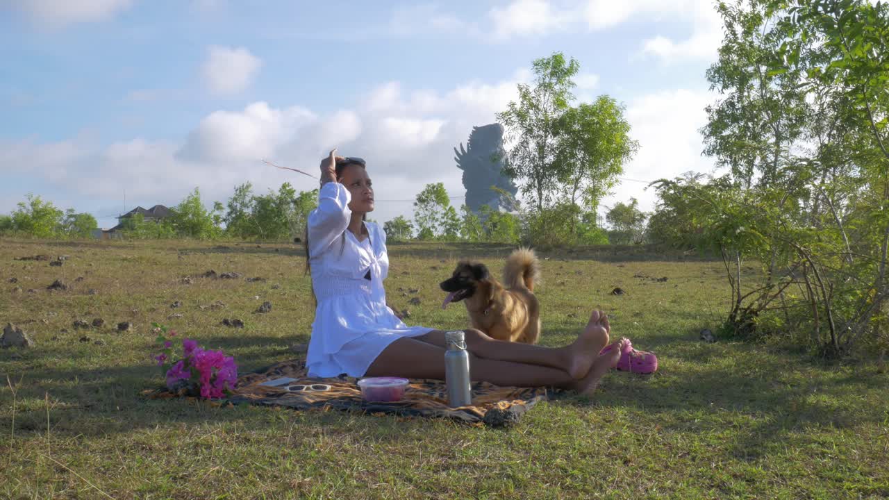 chica indonesia con vestido blanco haciendo un picnic con sus dos perros en un prado
