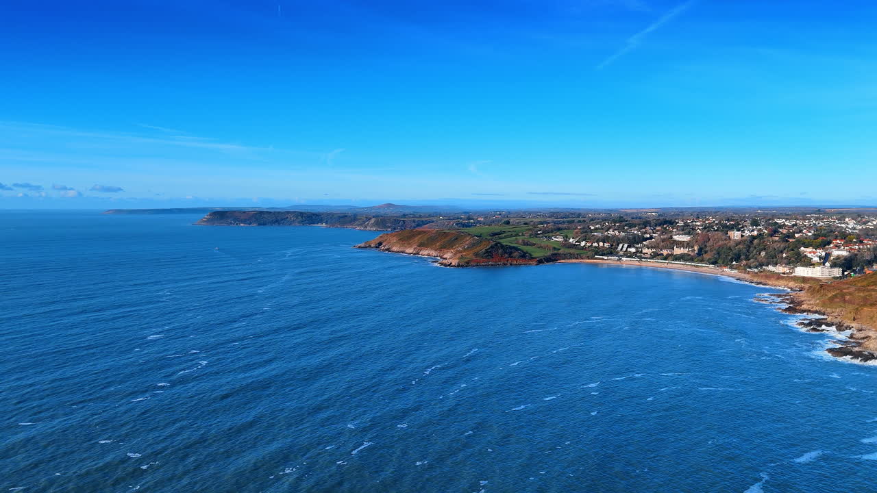 Ampio panorama del mare blu e della costa di Gower, Galles. Vista aerea panoramica di vaste acque oceaniche e promontori distanti sotto un cielo azzurro e limpido in Galles.