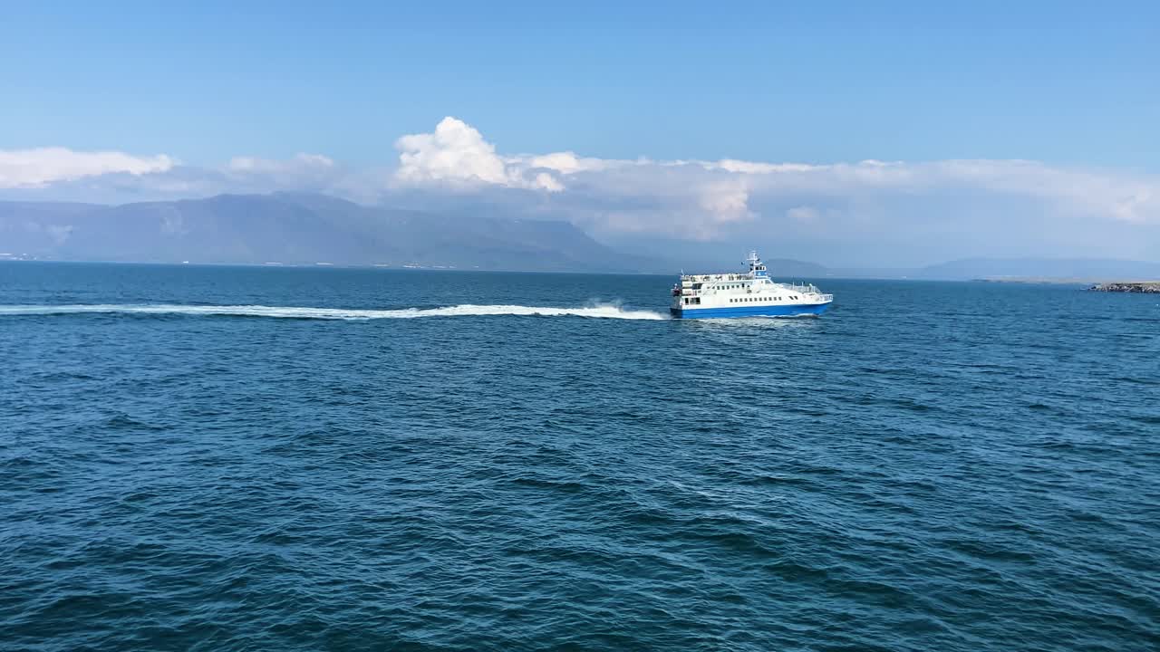 ferry azul cruzando las aguas islandesas con montañas bajo un cielo despejado, de día, tiro medio
