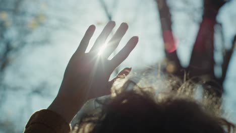 close up of woman with hand raised looking at the sun.