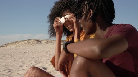 Vista-Lateral-De-Una-Pareja-Afroamericana-Jugando-Con-Conchas-En-La-Playa-4k