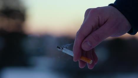 close-up of male caucasian hand holding a lit cigarette outdoors