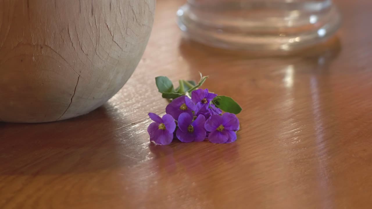 Närbild av livfulla lila blommor som vilar på en polerad träyta bredvid rustik keramik och glas, vilket framkallar en naturlig och fridfull atmosfär lämplig för hälso- och välmåendeteman.