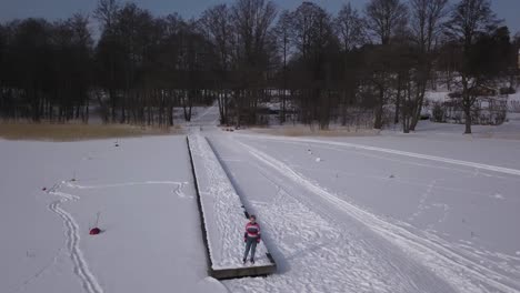 Smooth-tracking-dolly-aerial-shot-rotating-around-caucasian-female-standing-on-wooden-jetty-at-the-edge-of-vast-frozen-lake