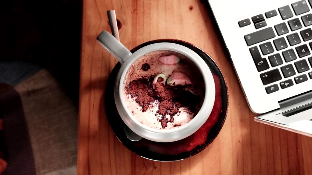 una grande tazza di cioccolato caldo con marshmallow accanto a un laptop su un tavolo