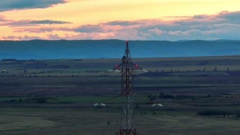 Ascending-aerial-shot-of-transmission-tower-on-farm-fields-in-front-of-mountain-range