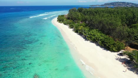 Beautiful-remote-exotic-beach-with-clear-blue-water-and-white-sand-captured-from-the-air-with-mountains-in-the-background