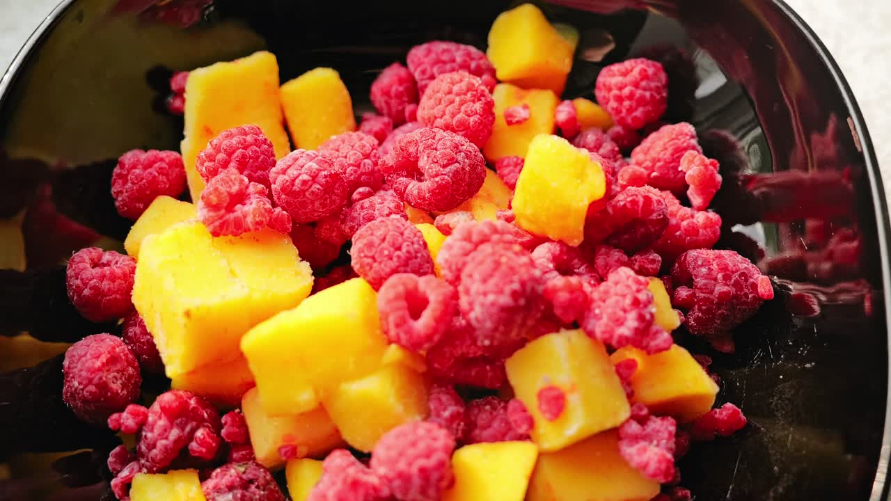 Vibrant frozen raspberries and yellow mango cubes served in glossy black bowl