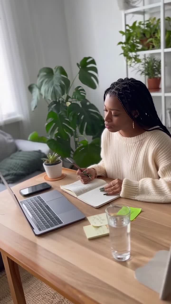 Overhead angle video of a woman writing at a desk, surrounded by plants in a cozy room