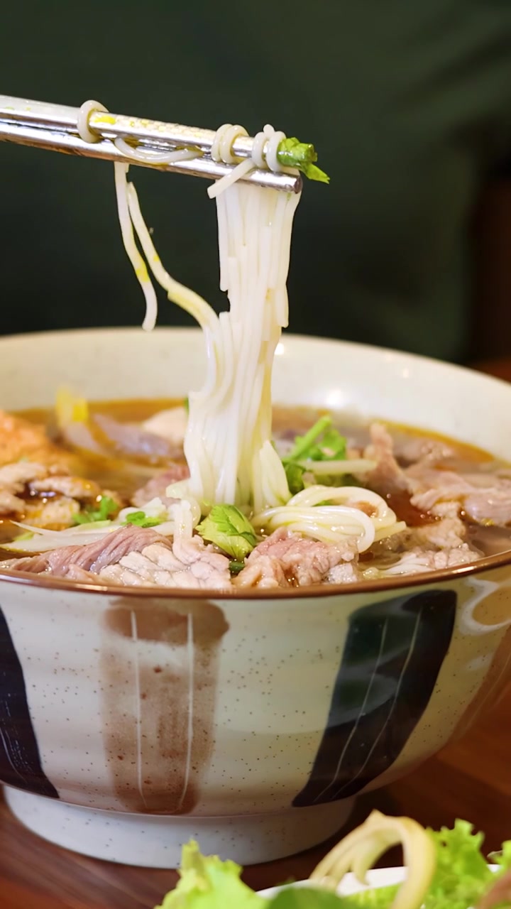 Một cảnh quay cận cảnh cho thấy một người đang gắp sợi phở từ một tô phở bò