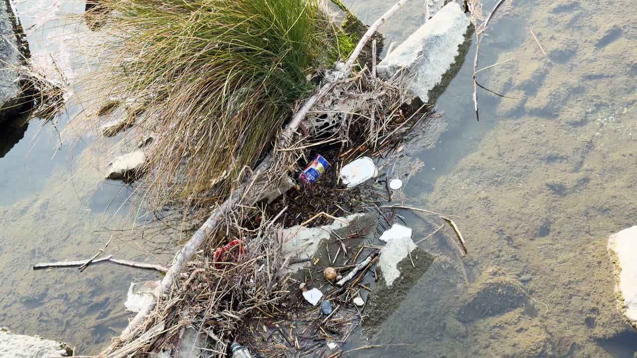 Un'inquadratura dall'alto mostra rifiuti di plastica e detriti sparsi lungo una riva rocciosa del fiume a Kyoto.
