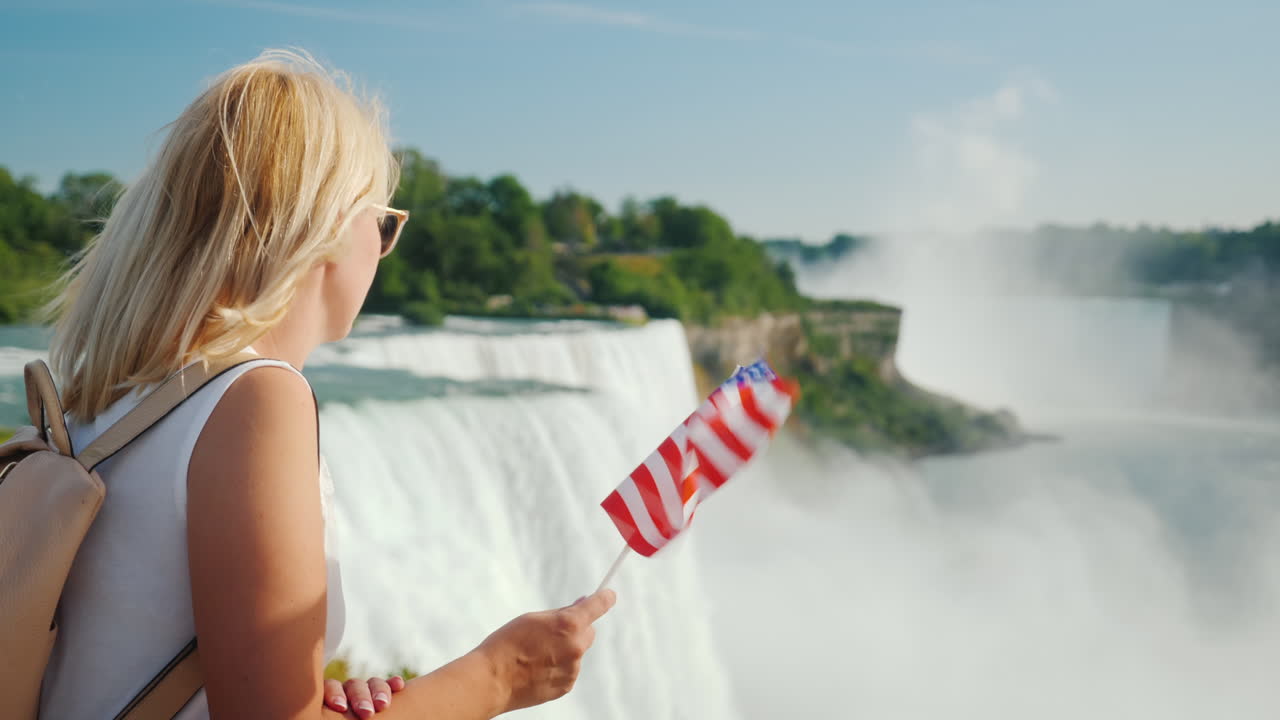 Traveling In The Usa - A Woman With The Flag Of America In Her Hand Admires Niagara Falls One Of The