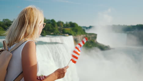 Reise-In-Die-Usa---Eine-Frau-Mit-Der-Flagge-Von-Amerika-In-Der-Hand-Bewundert-Die-Niagara-fälle-Einer-Der