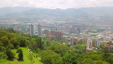 Toma-Panorámica-Aérea-De-Colinas-Y-Edificios-En-El-Centro-De-La-Ciudad-De-Medellín,-Mirador-Palmas