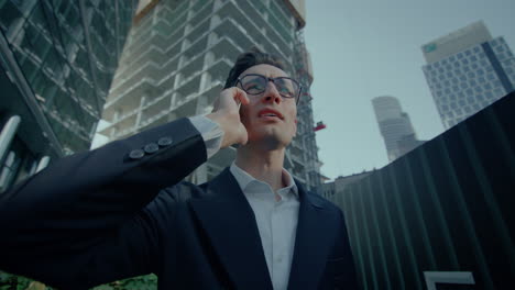 Low-angle-view-of-a-happy-business-man-talking-on-his-mobile-phone-with-office-view-at-background