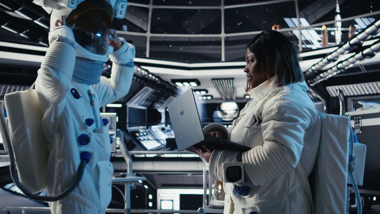 Astronauta di ritorno dalla superficie del pianeta si toglie il casco, parlando con un collega.