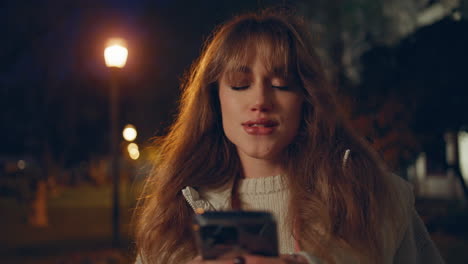 smiling girl checking cellphone under streetlights in street night city closeup.
