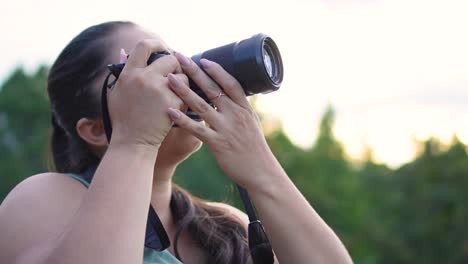 mujer con cámara dslr en sus manos, tomando fotos al aire libre con cielo brillante en el fondo