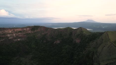 Cinemaic-Aerial-view-over-inactive-volcano-crater-covered-with-vegetation,-a-lake-and-another-volcano-on-the-background