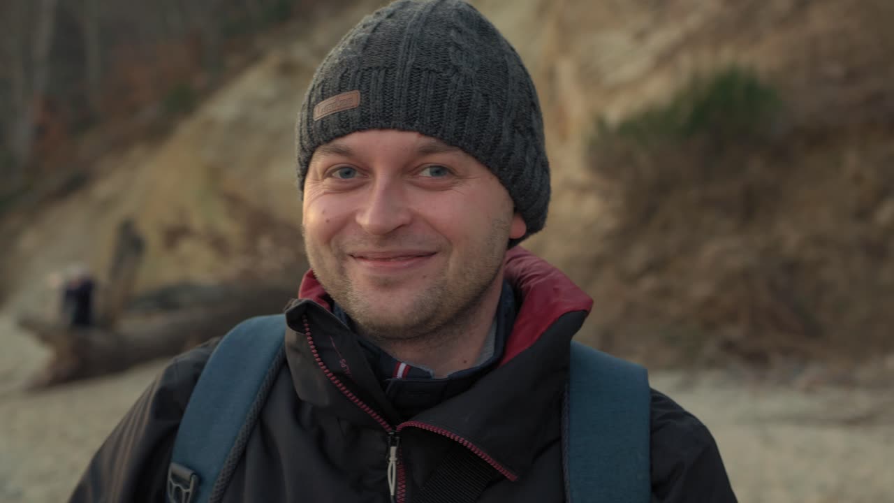 A medium angled shot of a man making jokes in front of the camera in front of a coastal background