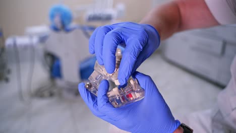 jaw model in hands. dentist showing on a jaw model how to put teeth where necessary. medic in blue gloves. close-up.