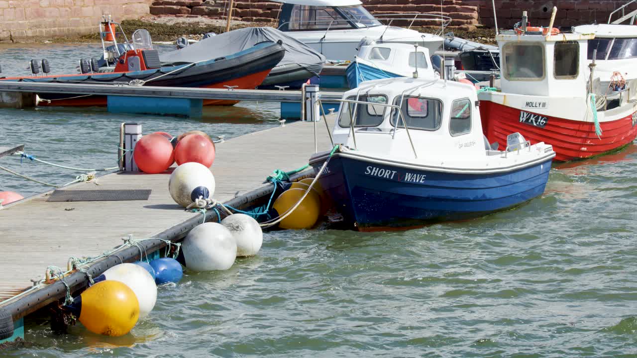 Small fishing boats rock on choppy water, moored to a dock in a bright harbour