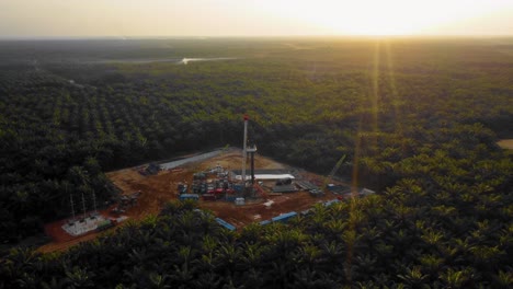 Cinematic-4K-Drone-Footage-of-Onshore-Drilling-Rig-equipment-structure-for-oil-exploration-and-exploitation-in-the-middle-of-jungle-surrounded-by-palm-oil-trees-during-sunset-and-high-oil-price