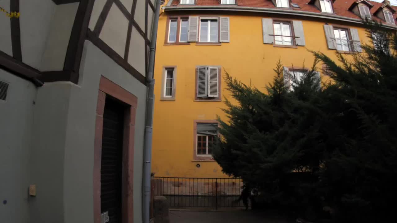 Low-angle footage of historic architecture in Colmar. Featuring a vibrant yellow building with traditional stone arches and shutters in the heart of France's Alsace region