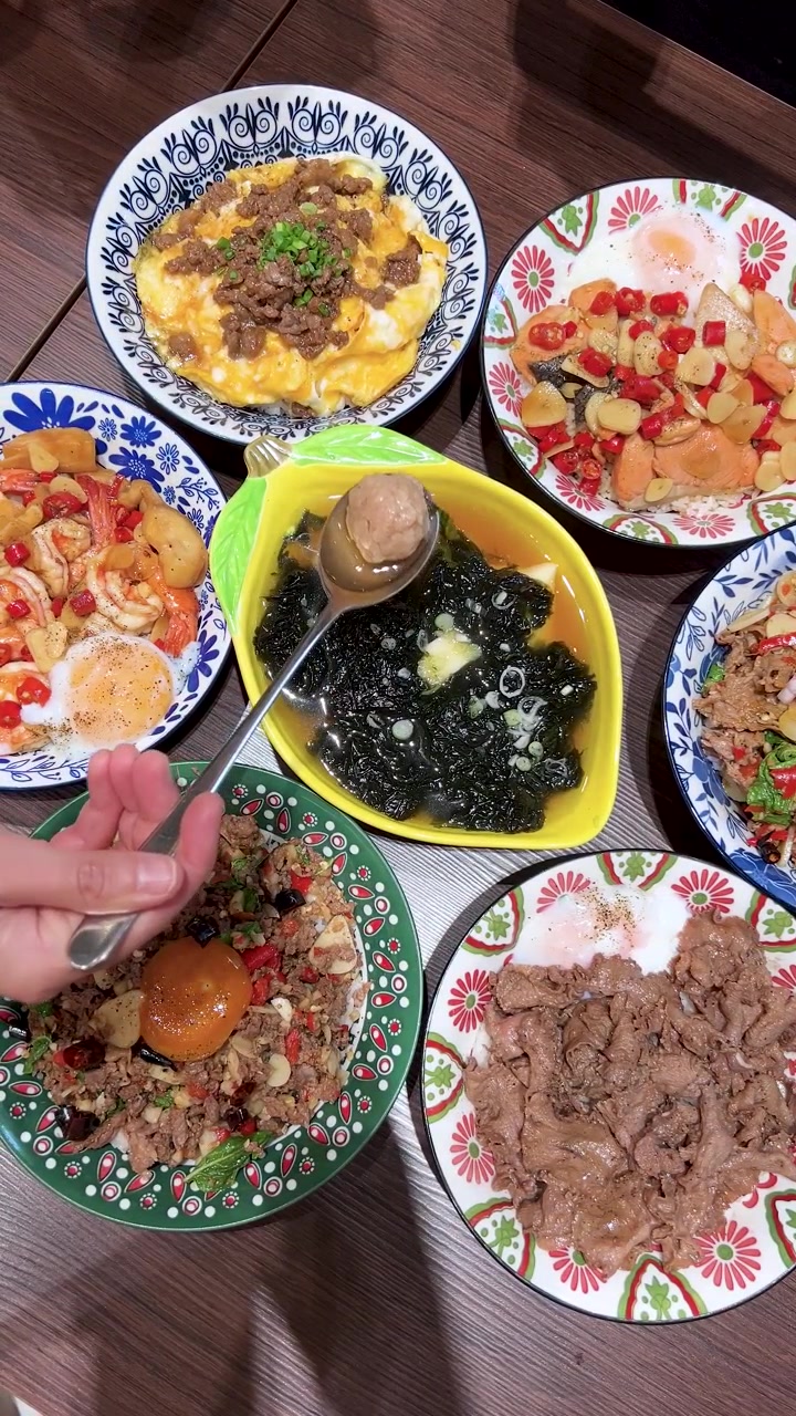 Ovenfra-perspektiv av en hånd som løfter en svinekjøttbolle fra en tangsuppe-skål, omgitt av fargerike thailandske retter under sterkt innendørs lys, stabilt kamera