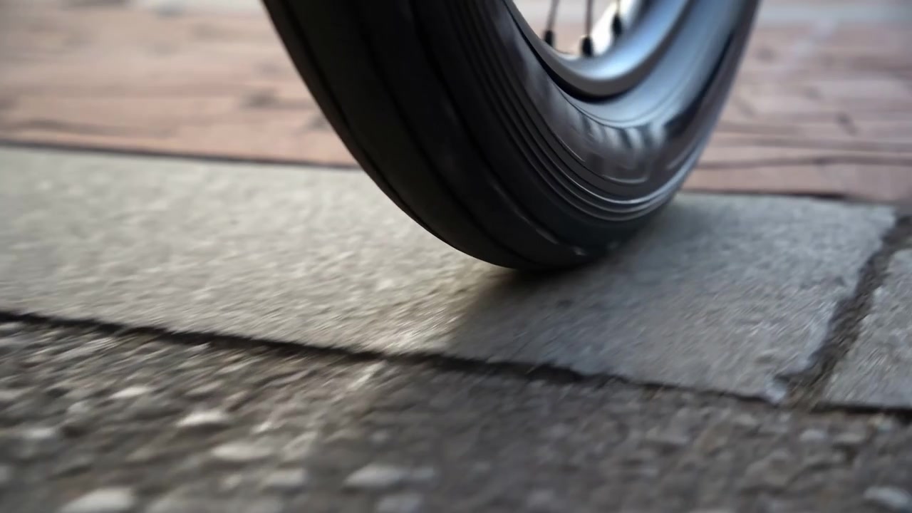 Primo piano di una ruota nera che si muove su una superficie pavimentata alla luce naturale del giorno, con uno sfondo leggermente sfocato e un movimento visibile sulla texture della strada.