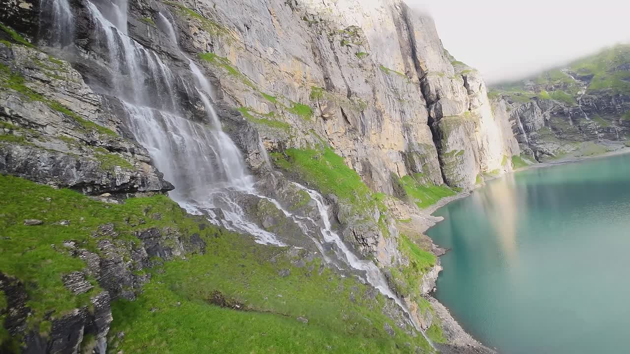 vuelo aéreo junto a una hermosa gran cascada en un paisaje montañoso, avión no tripulado volando sobre un lago azul - lago oeschinen, suiza
