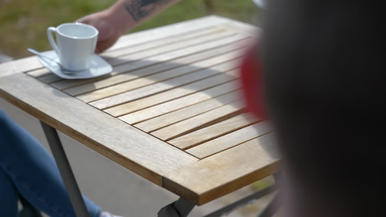 Person placerer tomme kaffekopper med underkopper på et træbord udendørs.