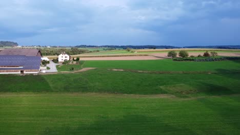 Drone-flying-over-green-fields-of-small-farm-in-countryside-in-Switzerland-,-clouds-look-like-it-will-rain