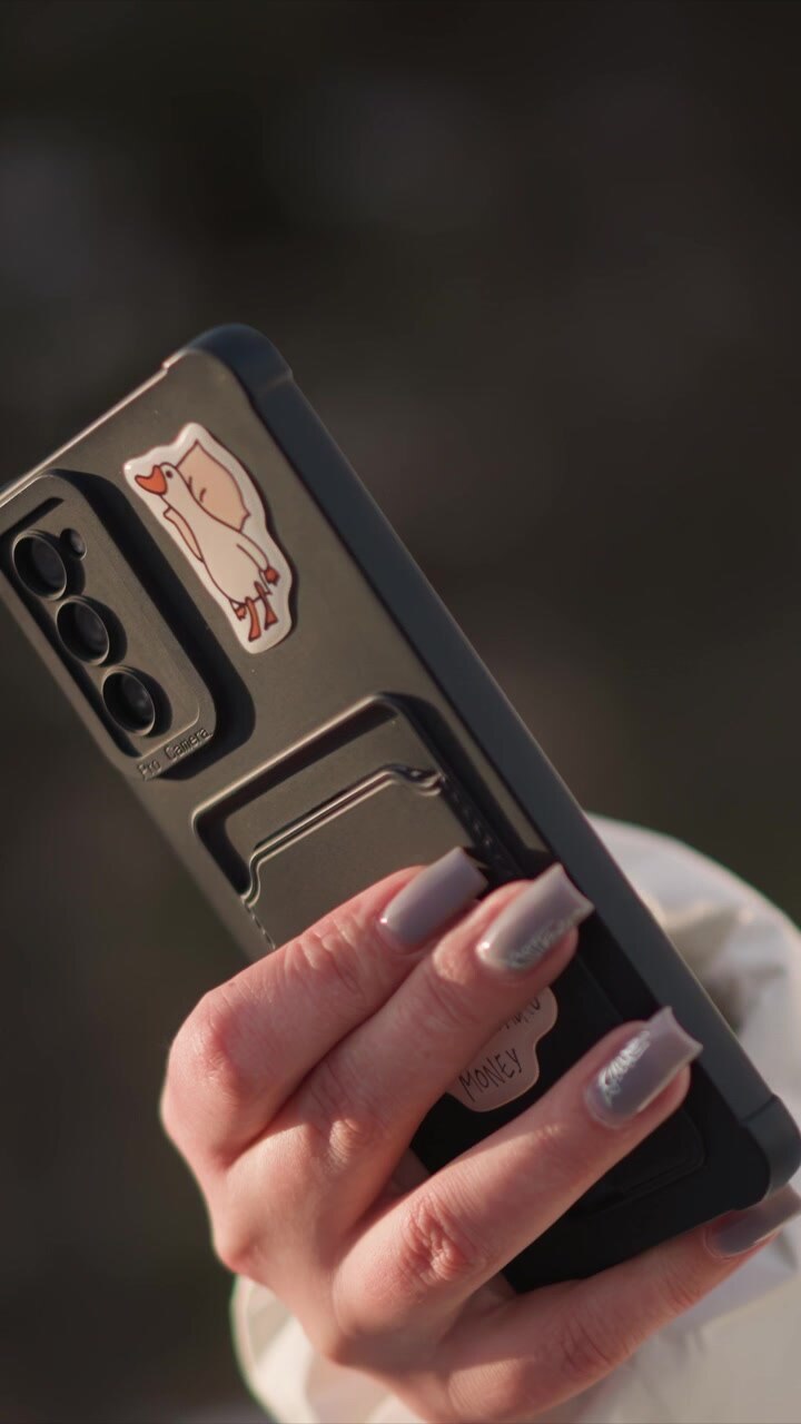 Una mano con smalto argentato regge uno smartphone che mostra il profilo laterale del dispositivo e il modulo fotocamera. Lo sfondo rimane leggermente sfocato, mettendo in risalto il primo piano delle dita che afferrano il telefono