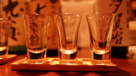 sake glasses being filled in sequence on shelf