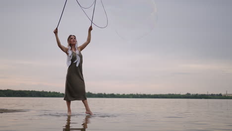 a young girl artist shows magic tricks using huge soap bubbles. create soap bubbles using sticks and rope at sunset to show a theatrical circus show