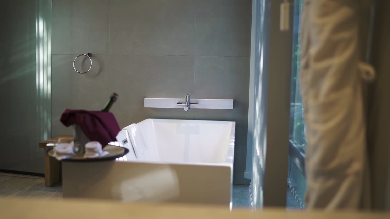 Stylish and contemporary hotel bathroom features a pristine white bathtub, a bottle of champagne chilling in an ice bucket, and soft lighting creating a luxurious and relaxing atmosphere, slow motion