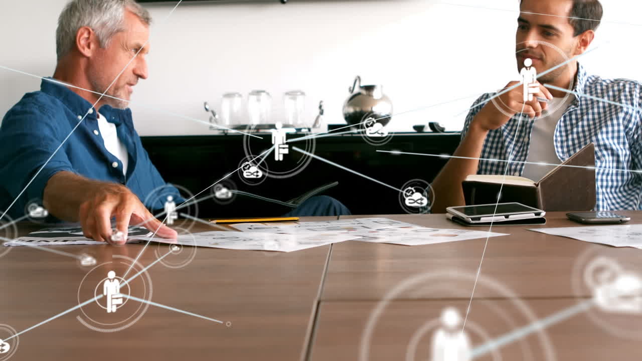 анимация сети цифровых икон над двумя белыми мужчинами, обсуждающими документы в офисе.