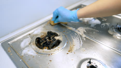 cleaning a dirty stovetop in a kitchen. a person uses a sponge to scrub a greasy stovetop, removing food residue and grime in a bright kitchen setting