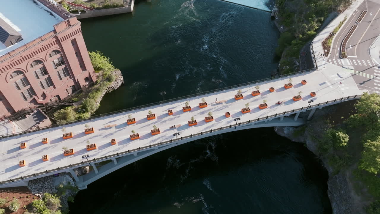 Overhead view of a white bridge crossing a river in downtown Spokane, next to a historic red-brick building