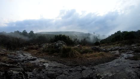 time lapse shot of mist from low hanging clouds pushing up and over a hillside rock face on a cold wet winter’s day, south africa