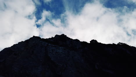 Silhouette-of-dark-rocky-hill-with-blue-sky-filled-with-clouds-in-background