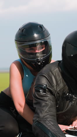young woman with beloved boyfriend biker rides modern motorbike along road past green trees and field at rural site in spring closeup slow motion