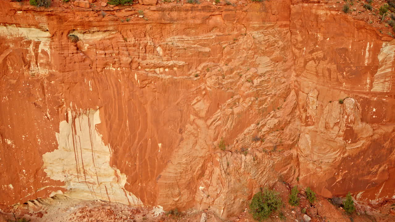 Drone glides along the face of a red rock canyon, revealing fascinating natural designs.