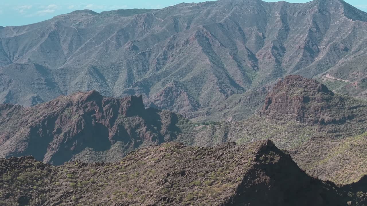 Aerial drone shot captures a massive, rugged mountain range with deep ridges and valleys, showcasing the dramatic volcanic landscape of Tenerife, Spain