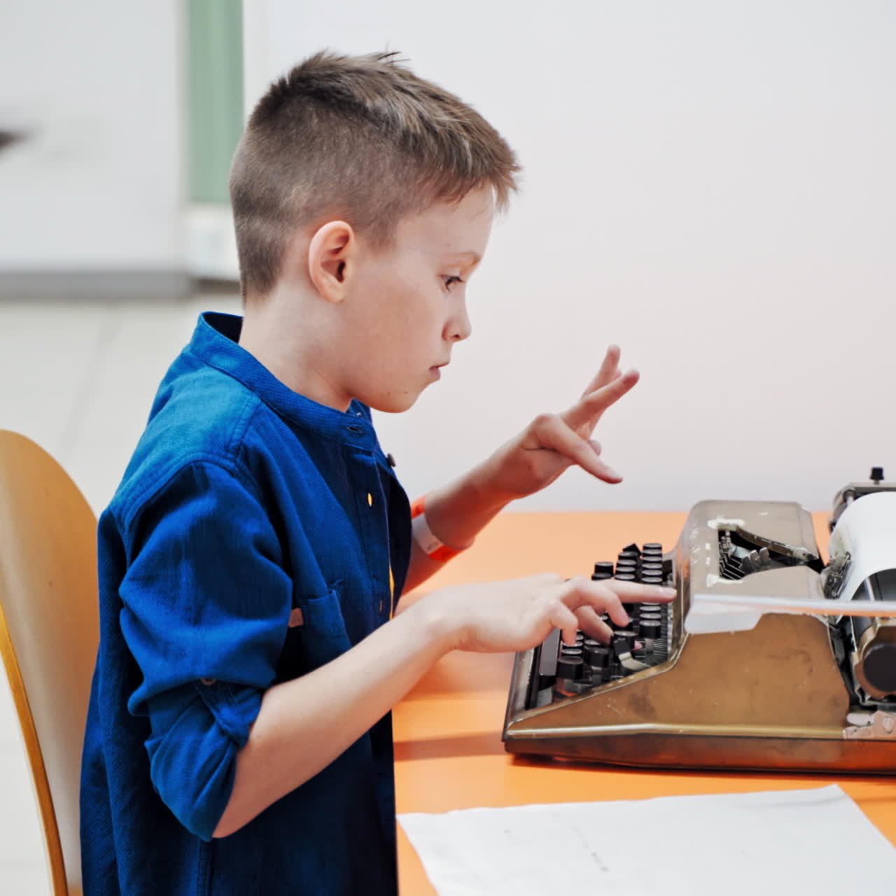 Boy sitting at table and typing old typewriter.