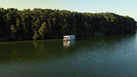 Houseboat-floating-on-a-green-natural-lake-next-to-an-island-in-Brandenburg,-Germany