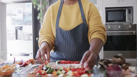 midsection of african american woman in apron preparing meal in kitchen, slow motion